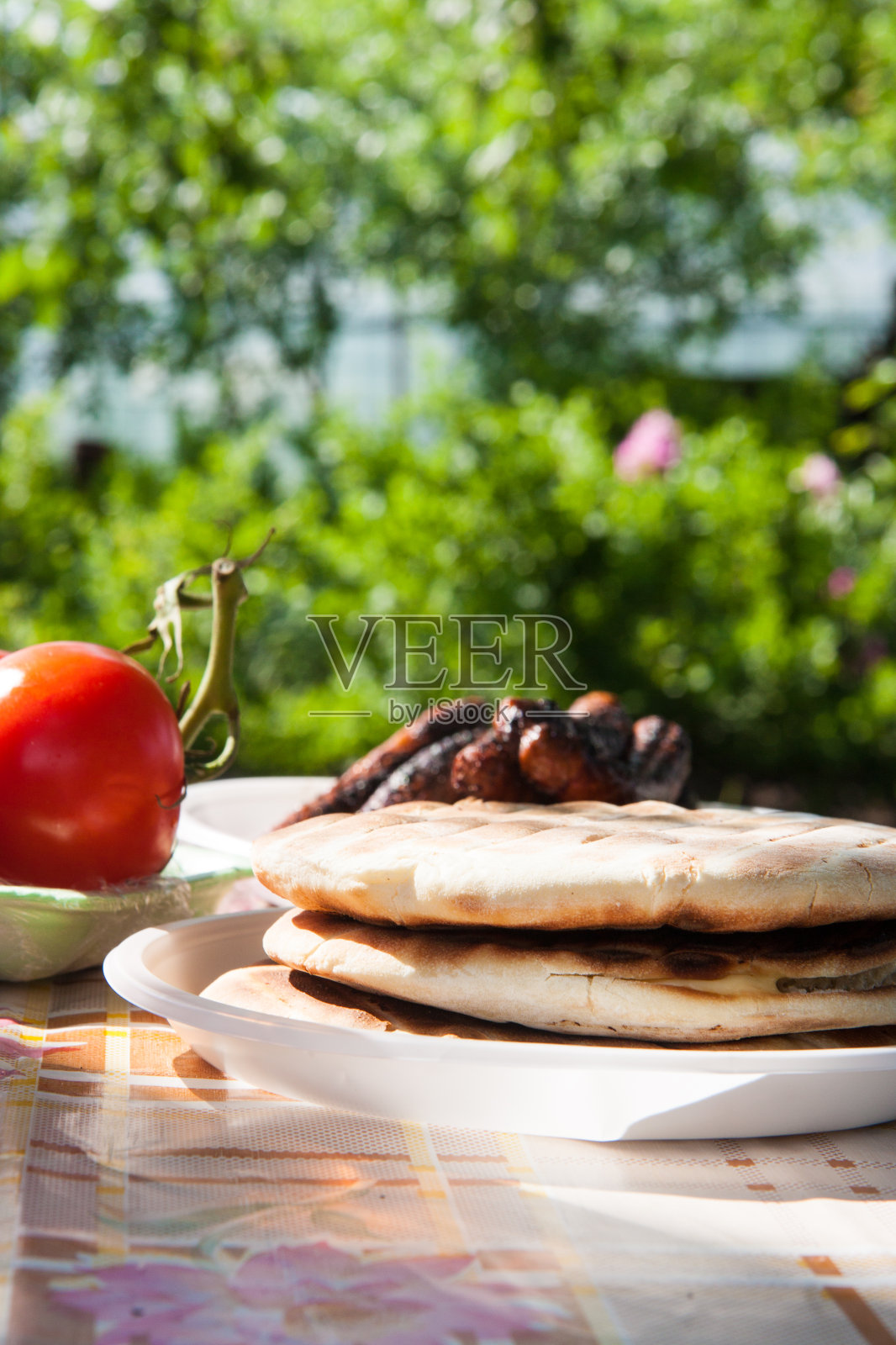 花园餐桌上的烤皮塔饼配肉和番茄。照片摄影图片