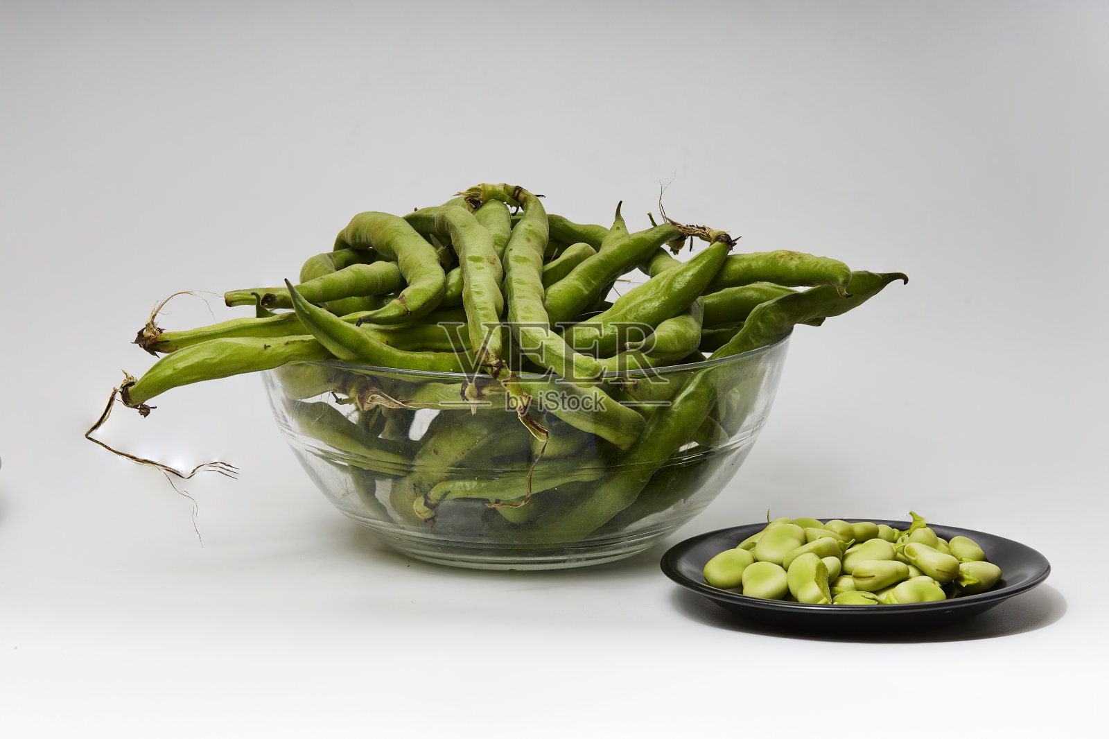 蚕豆切成两个黑色的盘子，在白色的背景上照片摄影图片