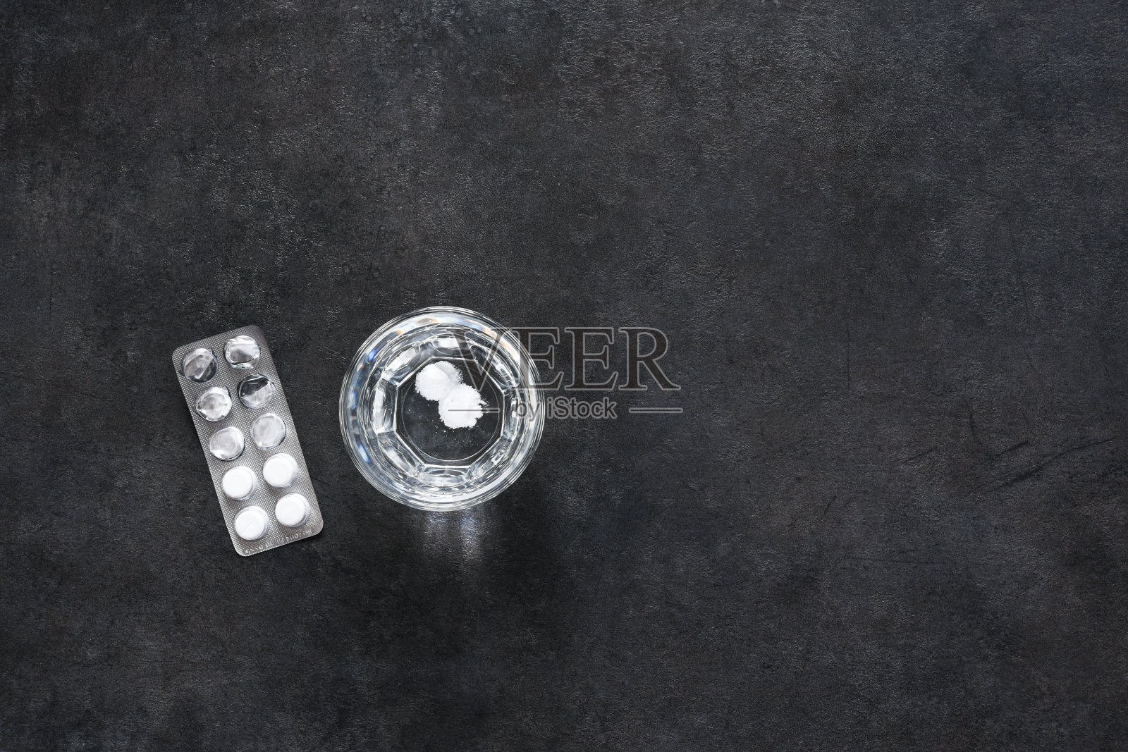 在混凝土背景上放着药片和一杯水。照片摄影图片
