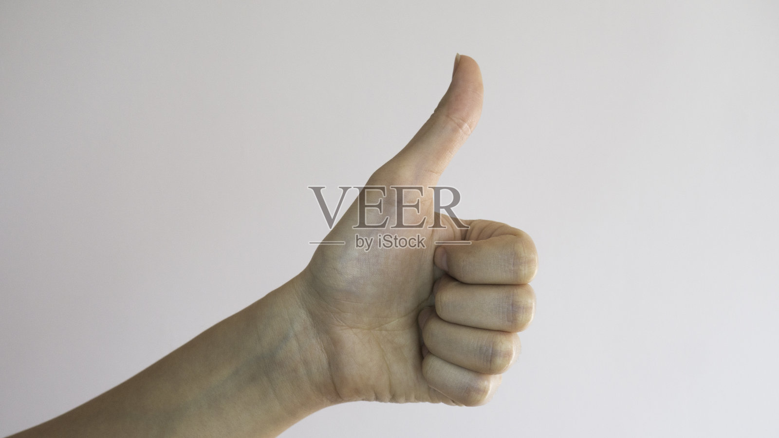 女性的左手。在白色背景上竖起大拇指。好的姿态。照片摄影图片