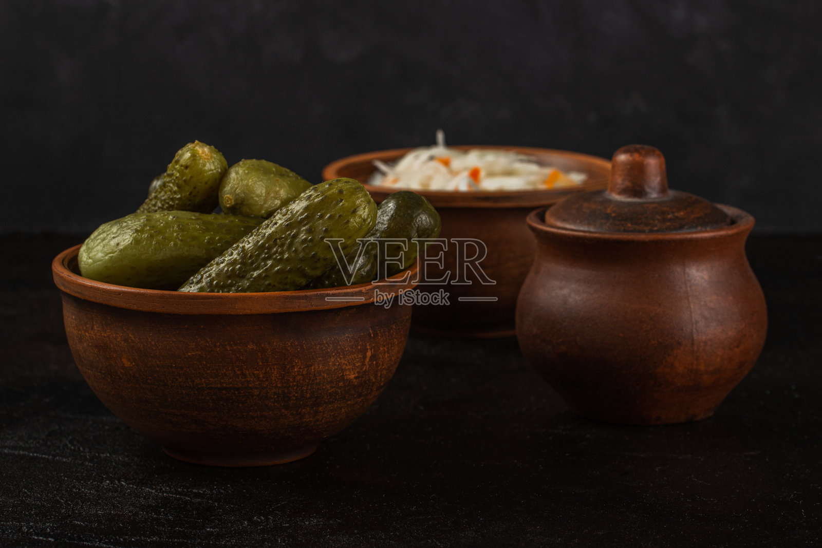 在黑色混凝土背景下，黏土碗里装着小黄瓜和泡菜照片摄影图片