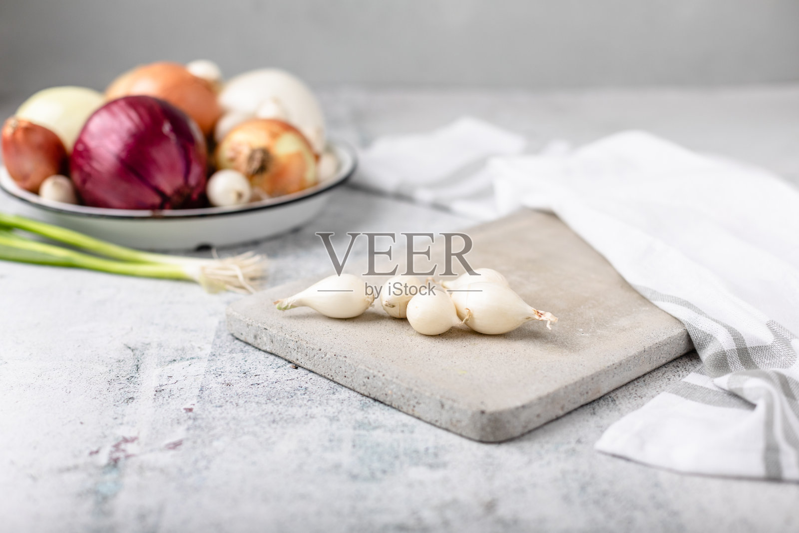 整颗珍珠洋葱在水泥切菜板上，背景中有几种洋葱失焦照片摄影图片