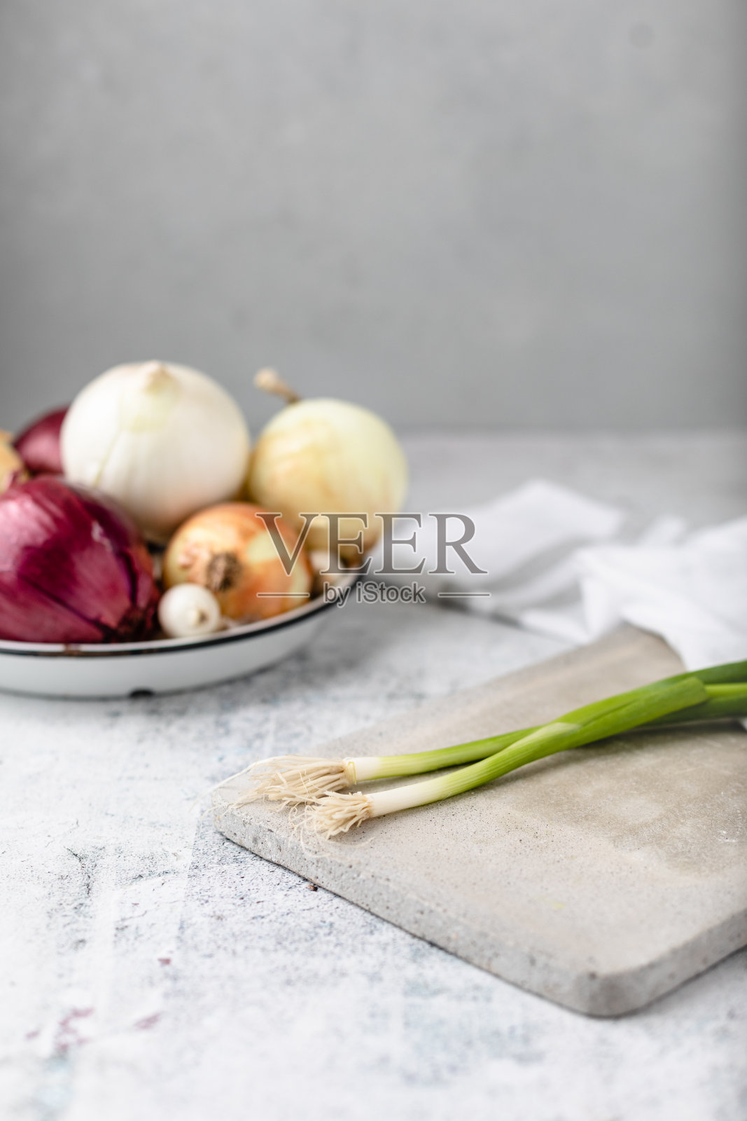 水泥切菜板上的整棵大葱，背景中几个品种的洋葱失去焦点照片摄影图片