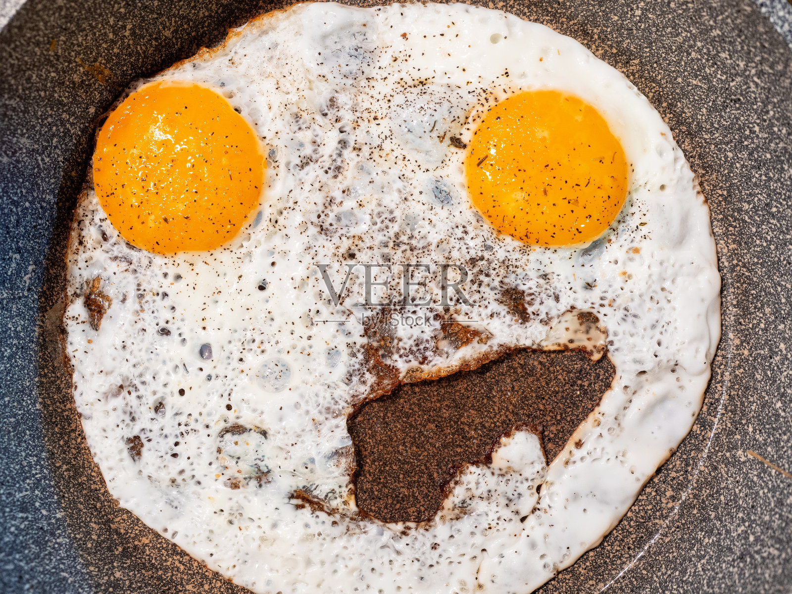 这是一张不寻常的煎蛋的特写照片，上面有两个类似表情符号的蛋黄照片摄影图片