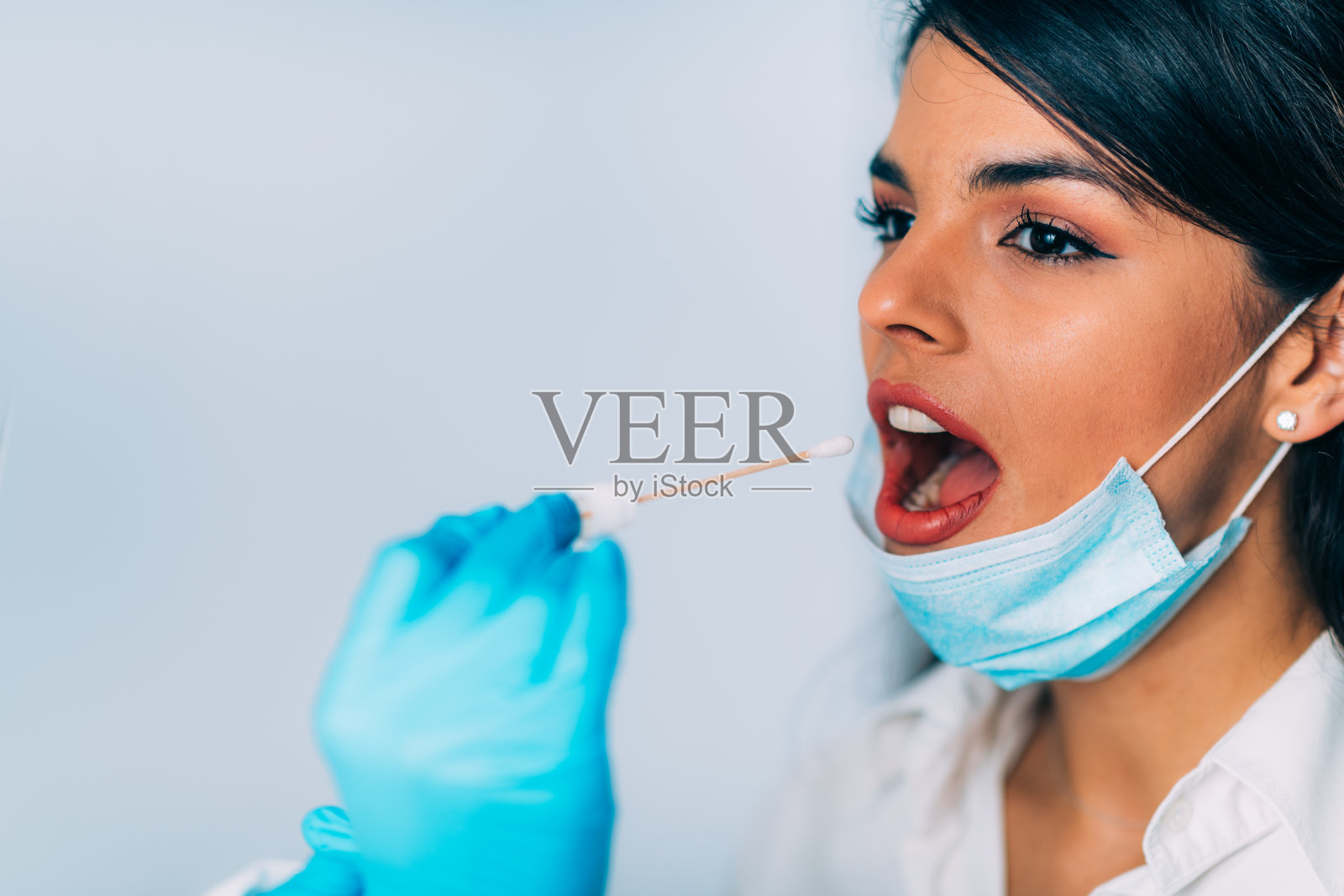 冠状病毒检测：穿防护服的医务人员为可能感染的年轻女性进行拭子取样照片摄影图片