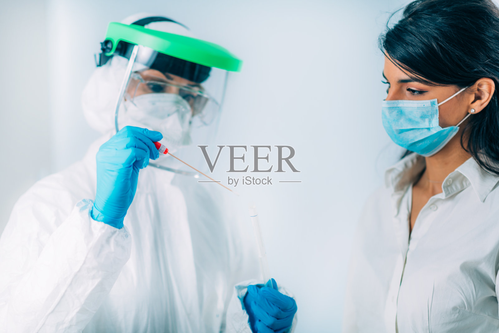 冠状病毒检测：穿防护服的医务人员为可能感染的年轻女性进行拭子取样照片摄影图片