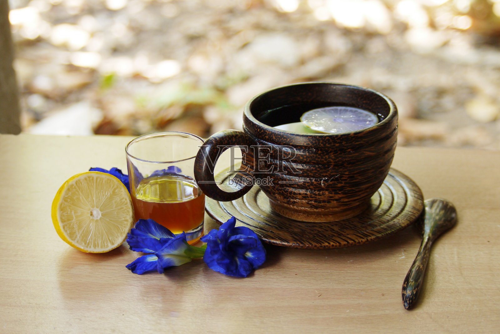 木桌上的木杯凉茶和勺子上的蝴蝶豌豆花和蜂蜜，选择性的重点。照片摄影图片