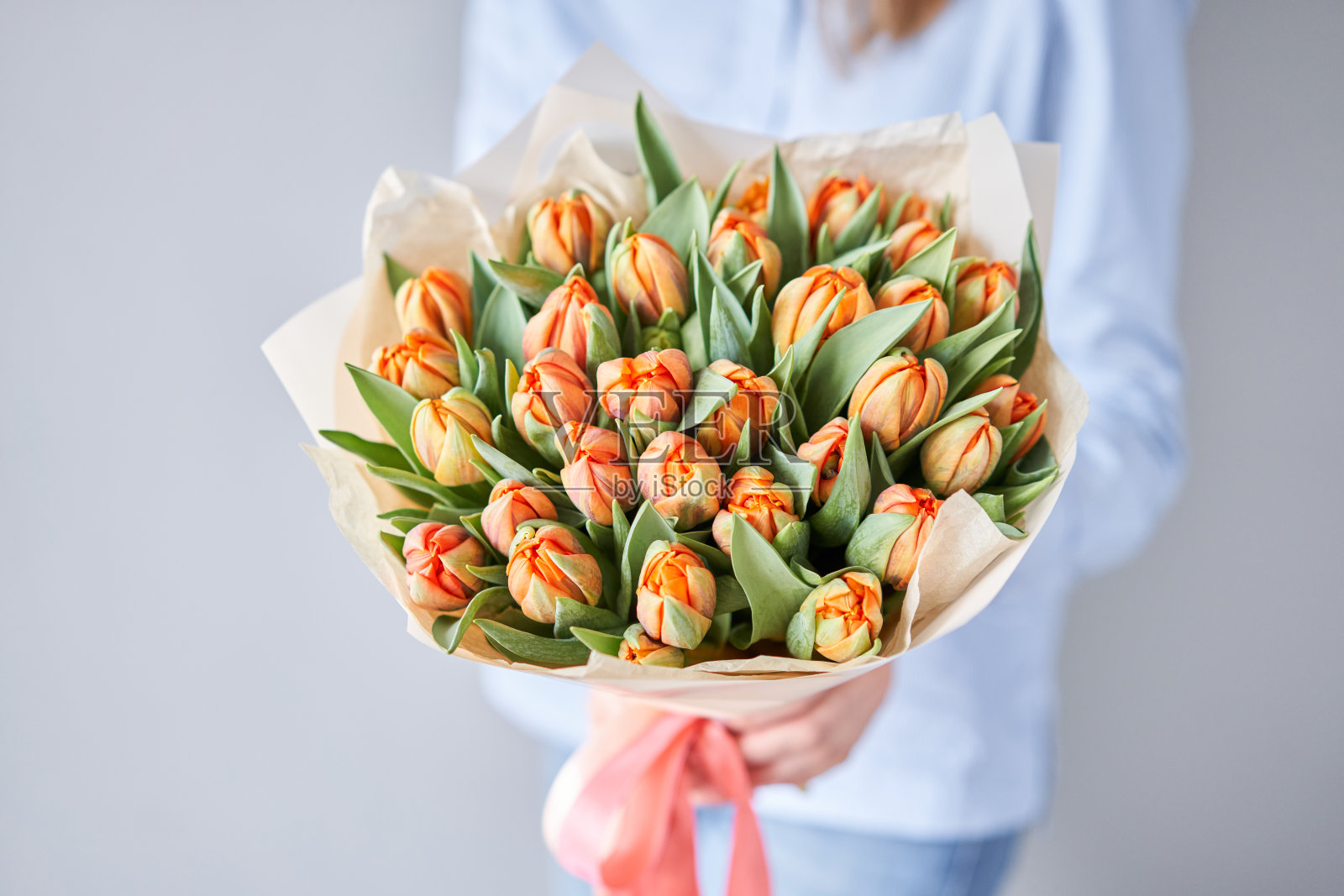 女人手里拿着橙色的郁金香。年轻漂亮的女人捧着春天的花束。女性手中捧着一束刚剪下来的春花照片摄影图片