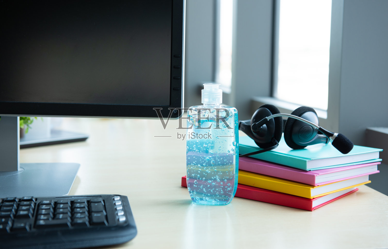 蓝色酒精凝胶洗手瓶与耳机放在工作场所的桌子上，防止细菌从冠状病毒或COVID-19病毒世界大流行，卫生保健和医学概念照片摄影图片