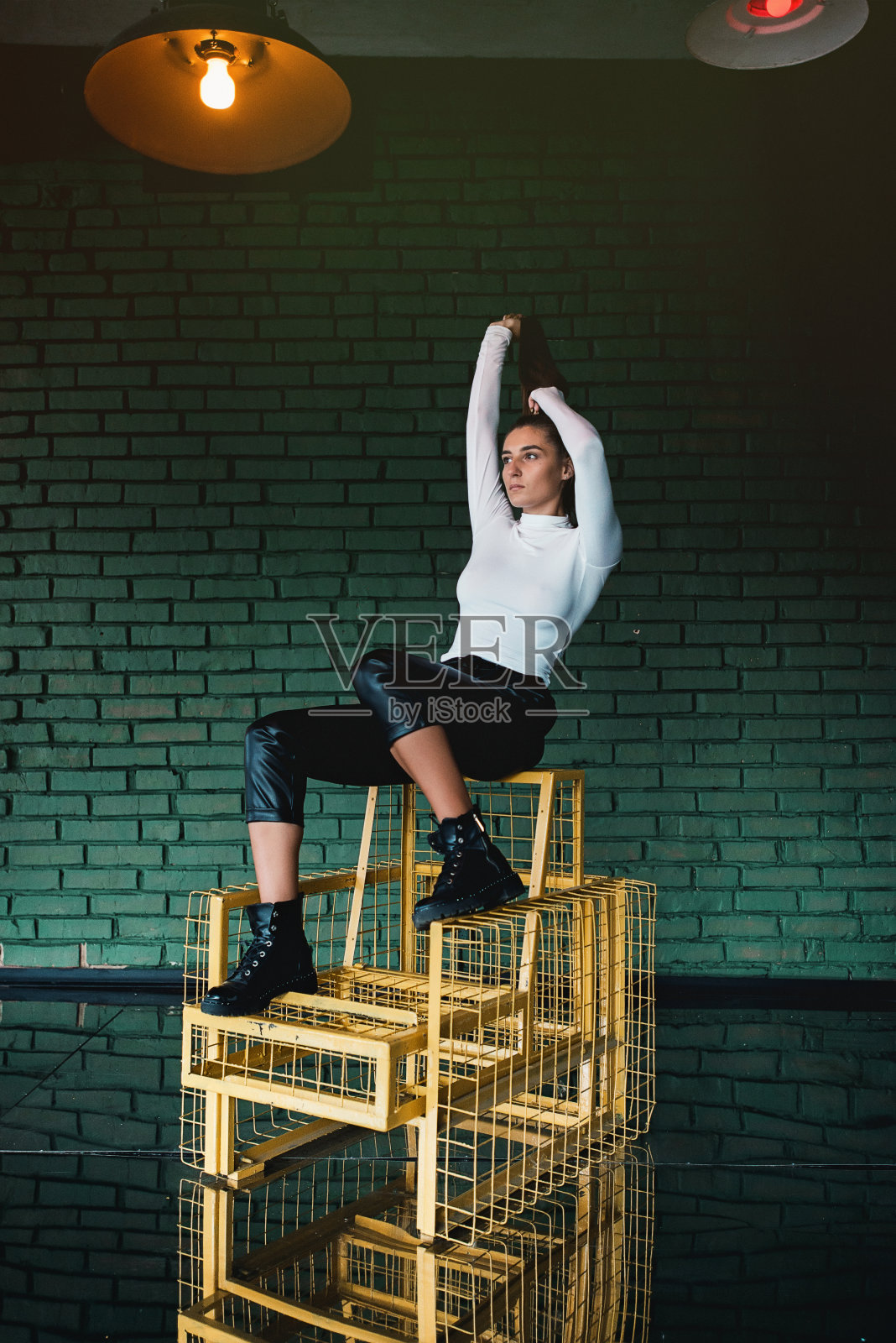 时尚的黑发女孩在白色毛衣和黑色皮裤摆姿势在绿色砖块的背景。照片摄影图片