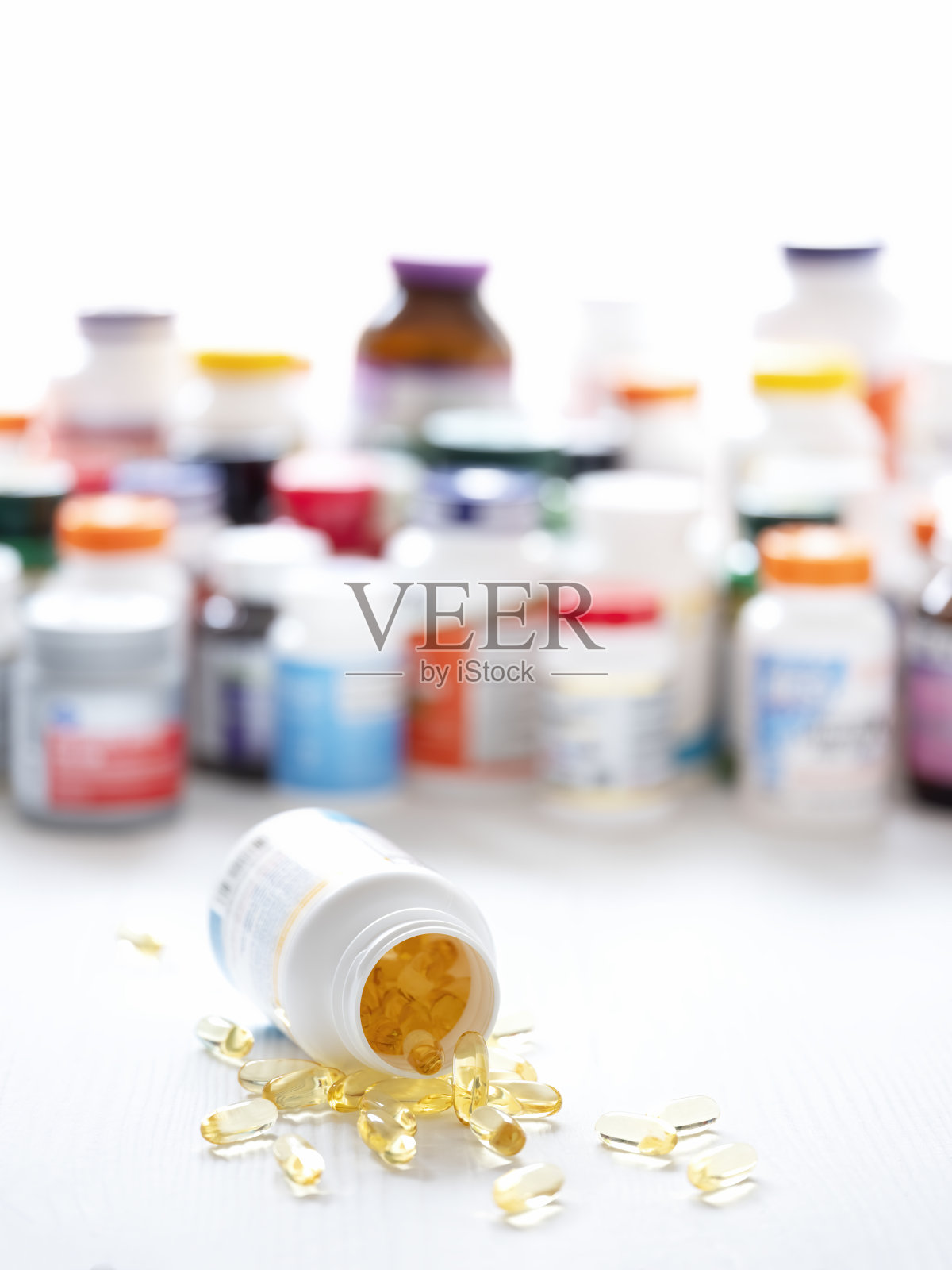 许多营养保健品的塑料瓶放在一个木制的背景上，一个瓶子躺在前景的焦点上，许多健康保健品的软明胶胶囊洒在桌子上。照片摄影图片