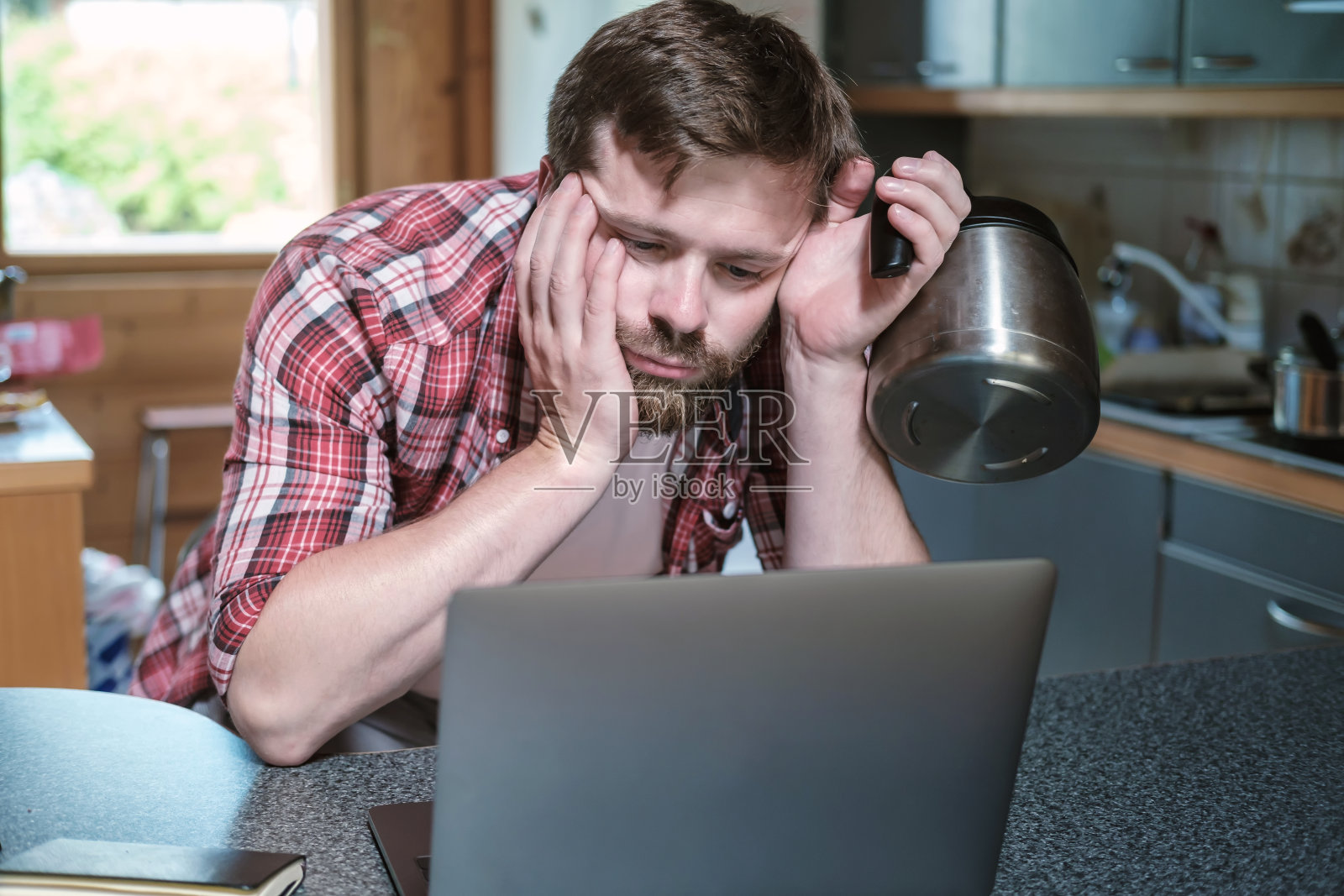 疲惫、过度劳累的男人睡眼惺忪地看着笔记本电脑，手里拿着咖啡壶照片摄影图片