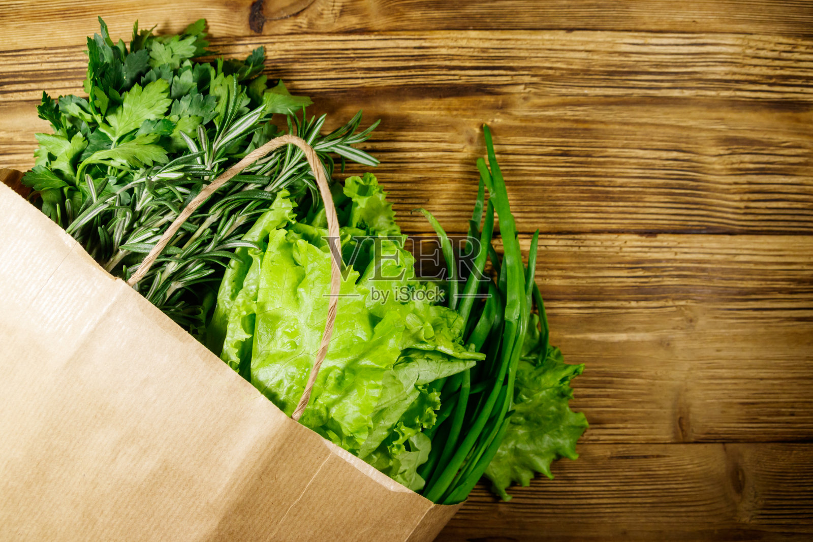 装着绿洋葱，迷迭香，莴苣叶和欧芹的纸袋放在木桌上。前视图。健康食品和杂货店购物的概念照片摄影图片