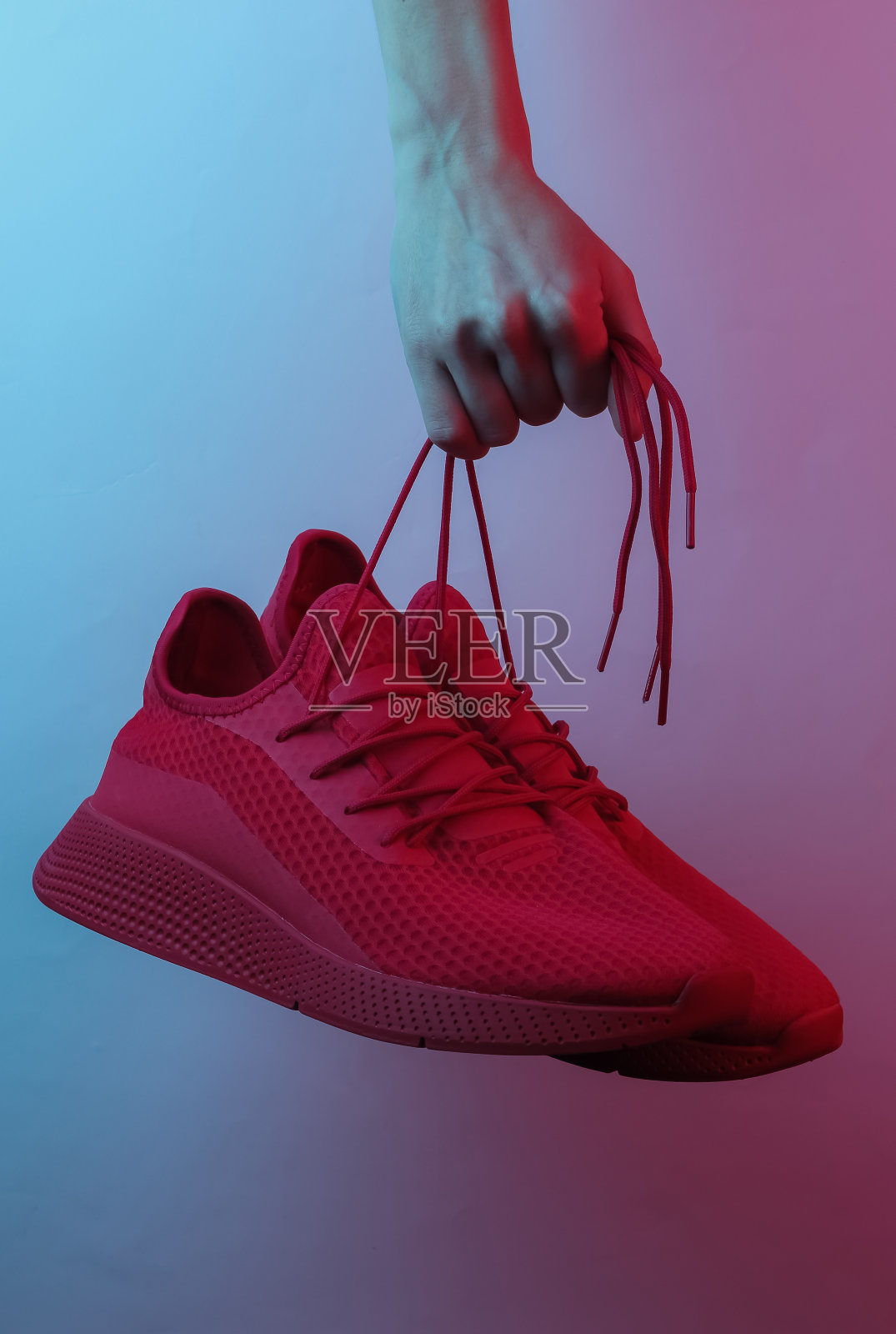 女人的手拿着红色运动鞋的鞋带。创意波普艺术粉蓝色霓虹色。时髦的梯度照明。夜灯照片摄影图片