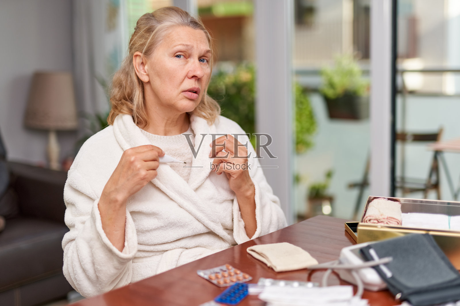 疾病、季节性病毒问题概念。一位忧心忡忡的老妇人测量着房子的温度照片摄影图片