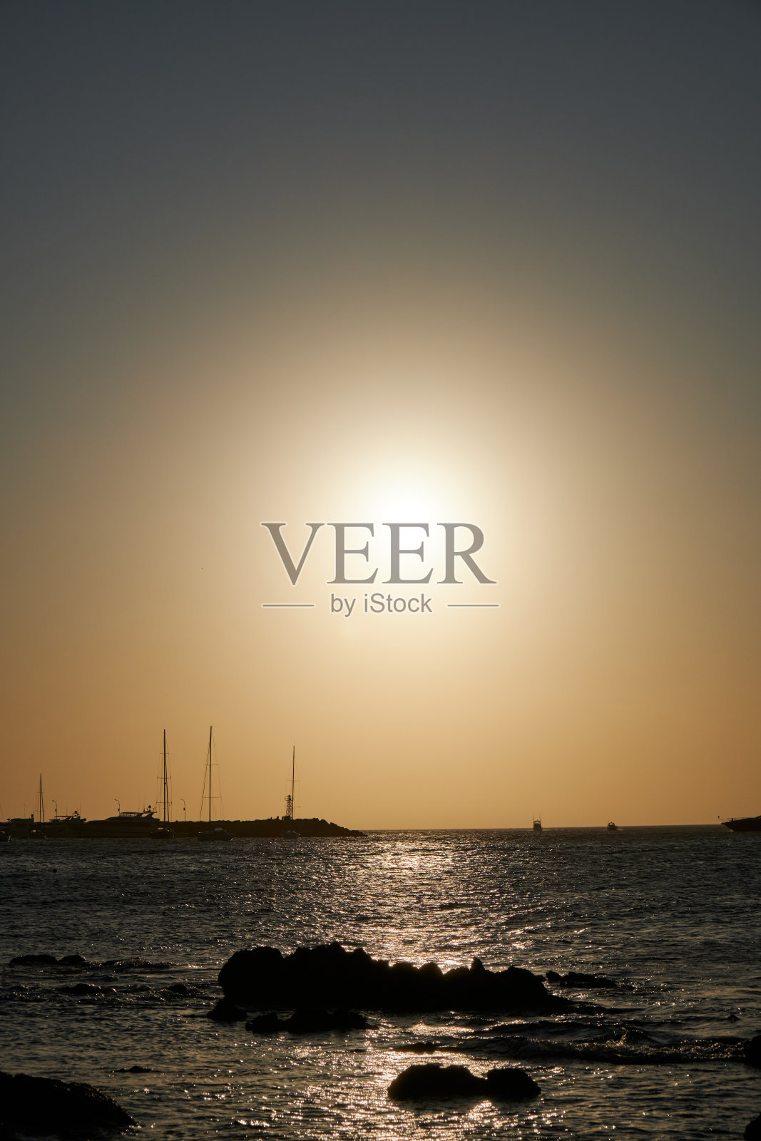 在埃斯特角港的岩石上，小船和帆船后面的大西洋夕阳照片摄影图片