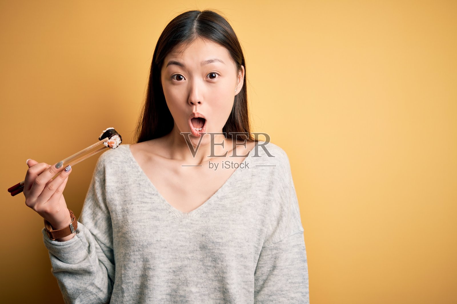 年轻的亚洲女子吃着日本食物，用筷子拿着三文鱼和寿司米饭吓得一脸惊讶，害怕又兴奋又害怕的表情照片摄影图片