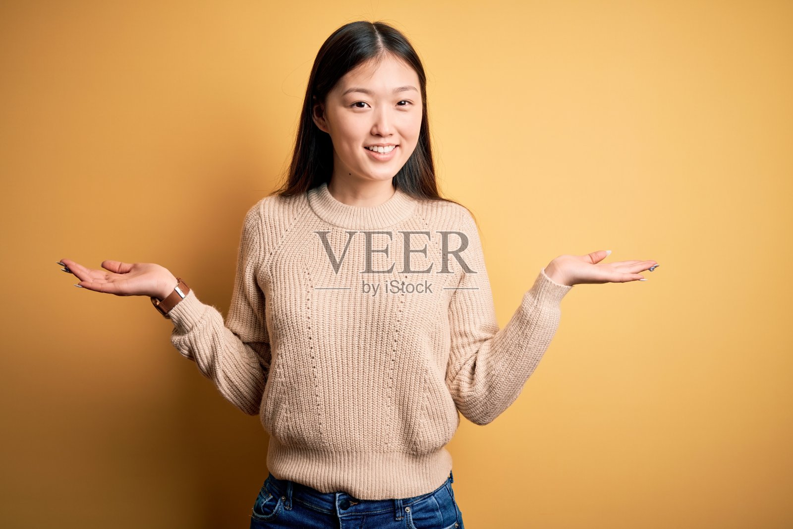 年轻美丽的亚洲女人穿着休闲毛衣在黄色孤立的背景微笑显示双手张开的手掌，呈现和广告比较和平衡照片摄影图片