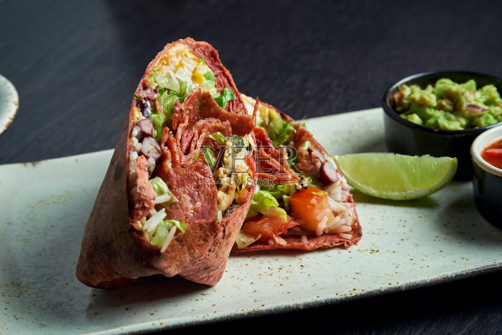 近距离观看墨西哥卷与意大利香肠，米饭，西红柿，玉米和甜椒在棕色皮塔饼在一个棕色盘子与番茄莎莎和鳄梨酱。素食主义者吃沙瓦玛卷照片摄影图片