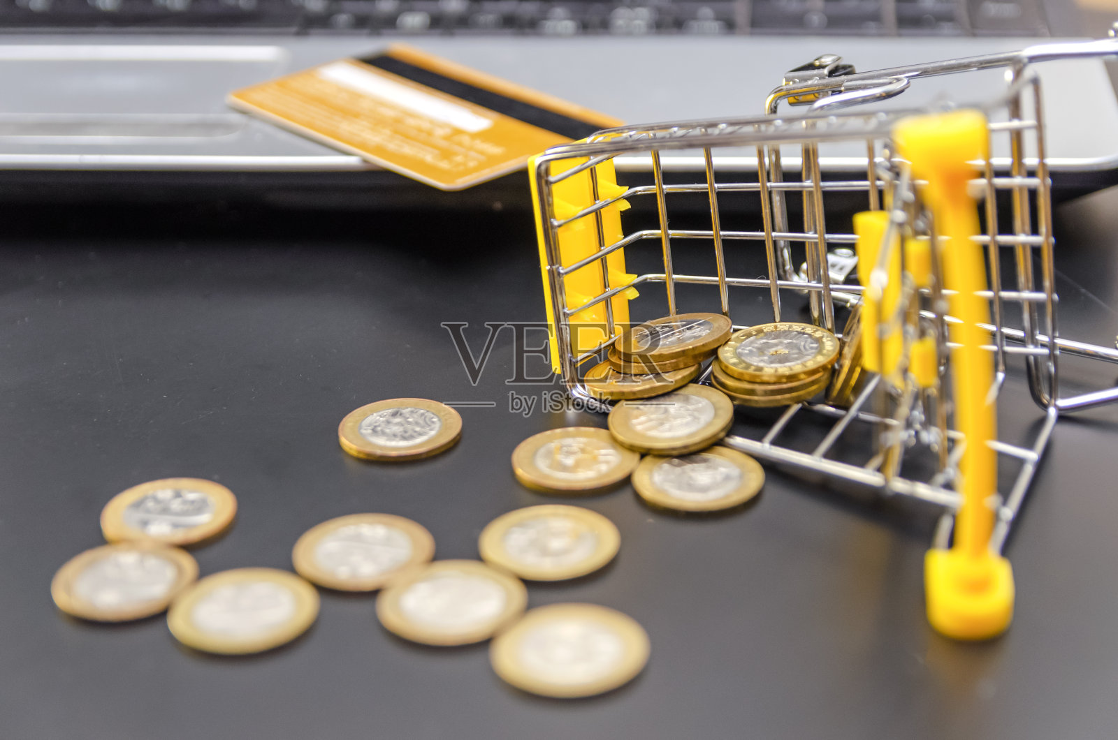 购物车与零散的金币和信用卡附近的笔记本电脑特写。网上购物的概念，赊账购物照片摄影图片