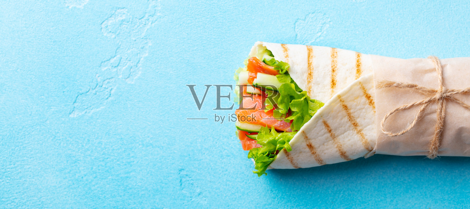 包上三明治，卷上鱼、鲑鱼和蔬菜。蓝色背景。副本的空间。前视图。照片摄影图片