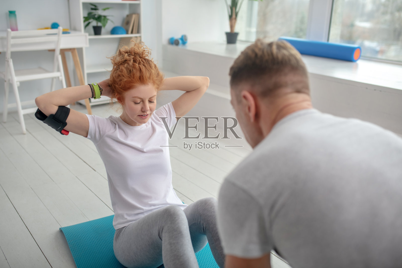 女患者在垫子上做仰卧起坐，男理疗师按住她的脚踝照片摄影图片