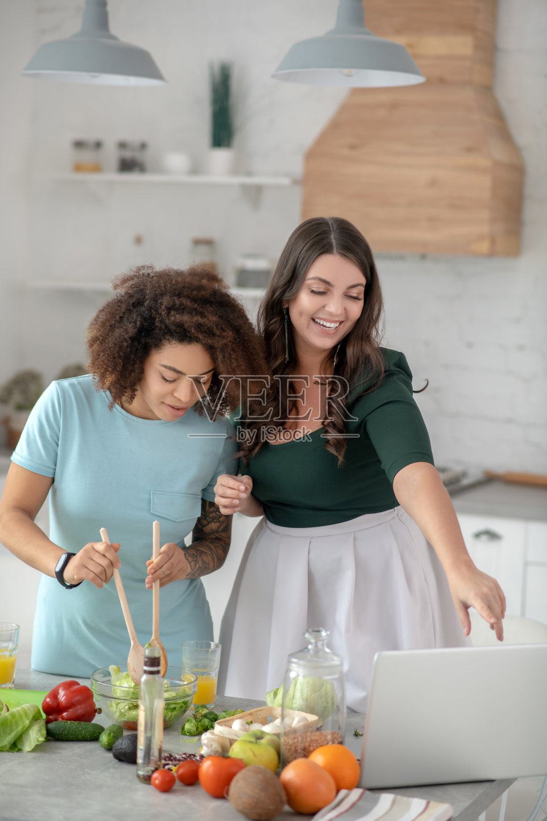 女人搅拌沙拉，另一个人看着笔记本电脑屏幕照片摄影图片