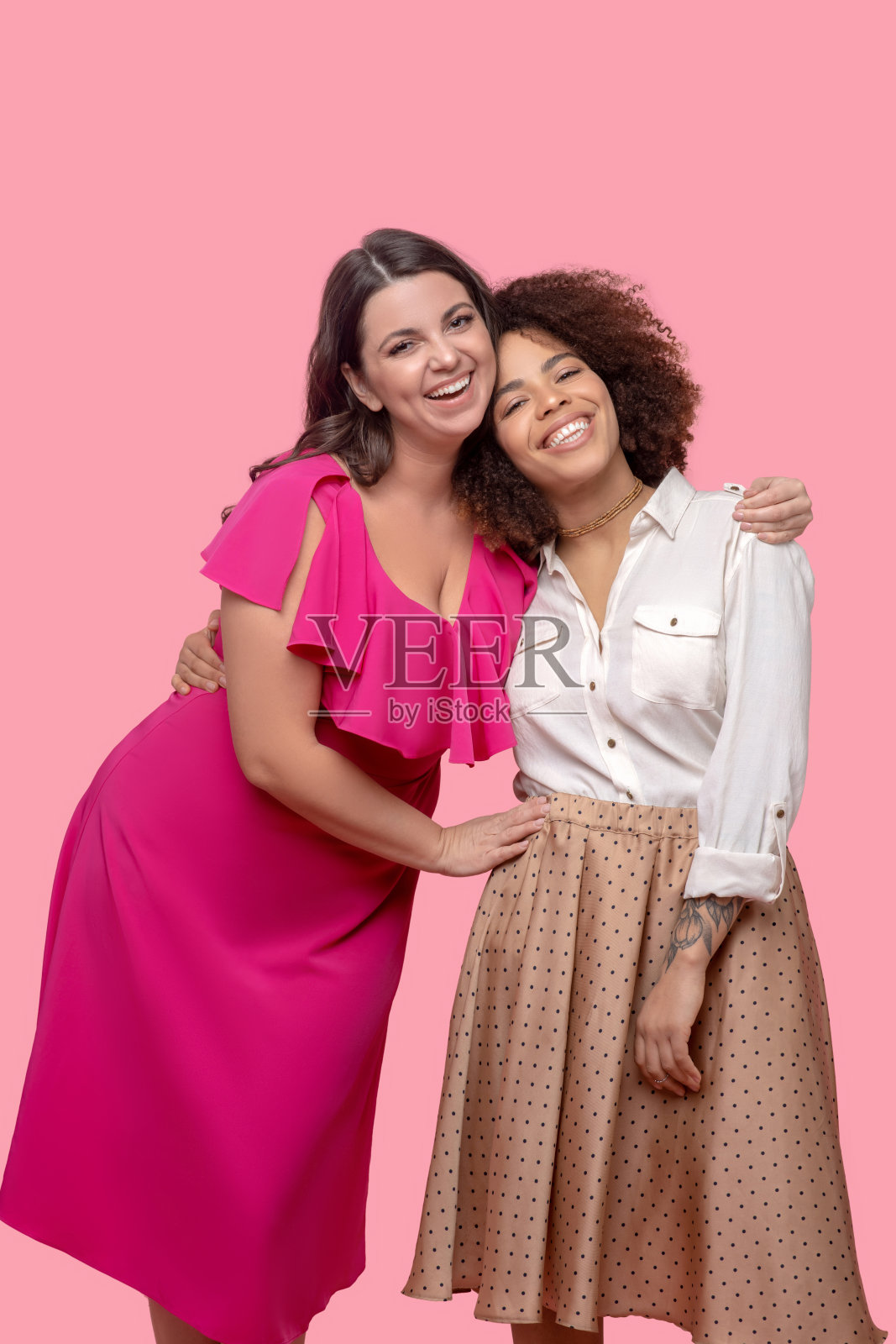 两位穿着漂亮衣服的年轻女人拥抱在一起。照片摄影图片