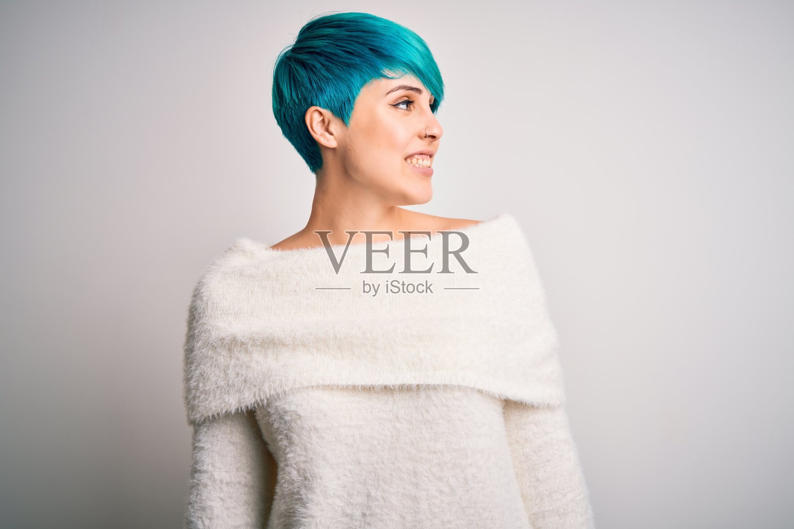 年轻美丽的女人与蓝色时尚的头发穿着休闲毛衣在白色的背景看向一边与微笑的脸，自然的表情。自信的笑。照片摄影图片