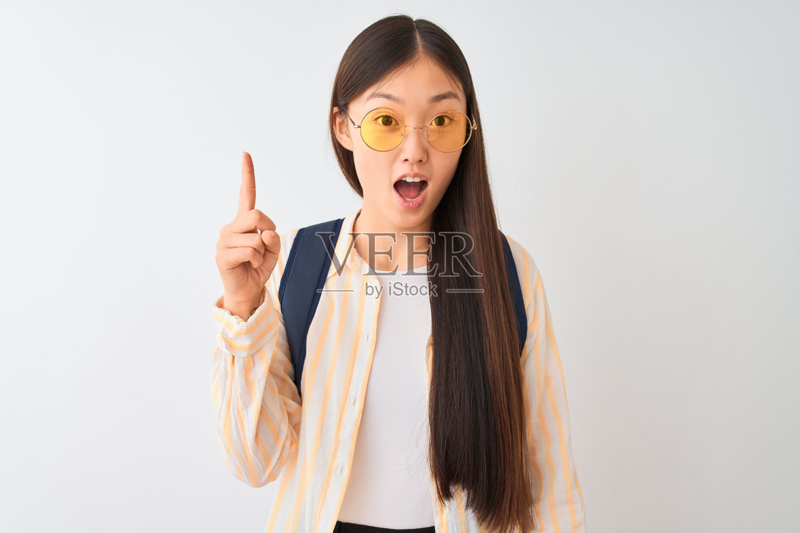 年轻的中国女学生戴着眼镜和背包在孤立的白色背景指向成功的想法。退出和快乐。第一。照片摄影图片