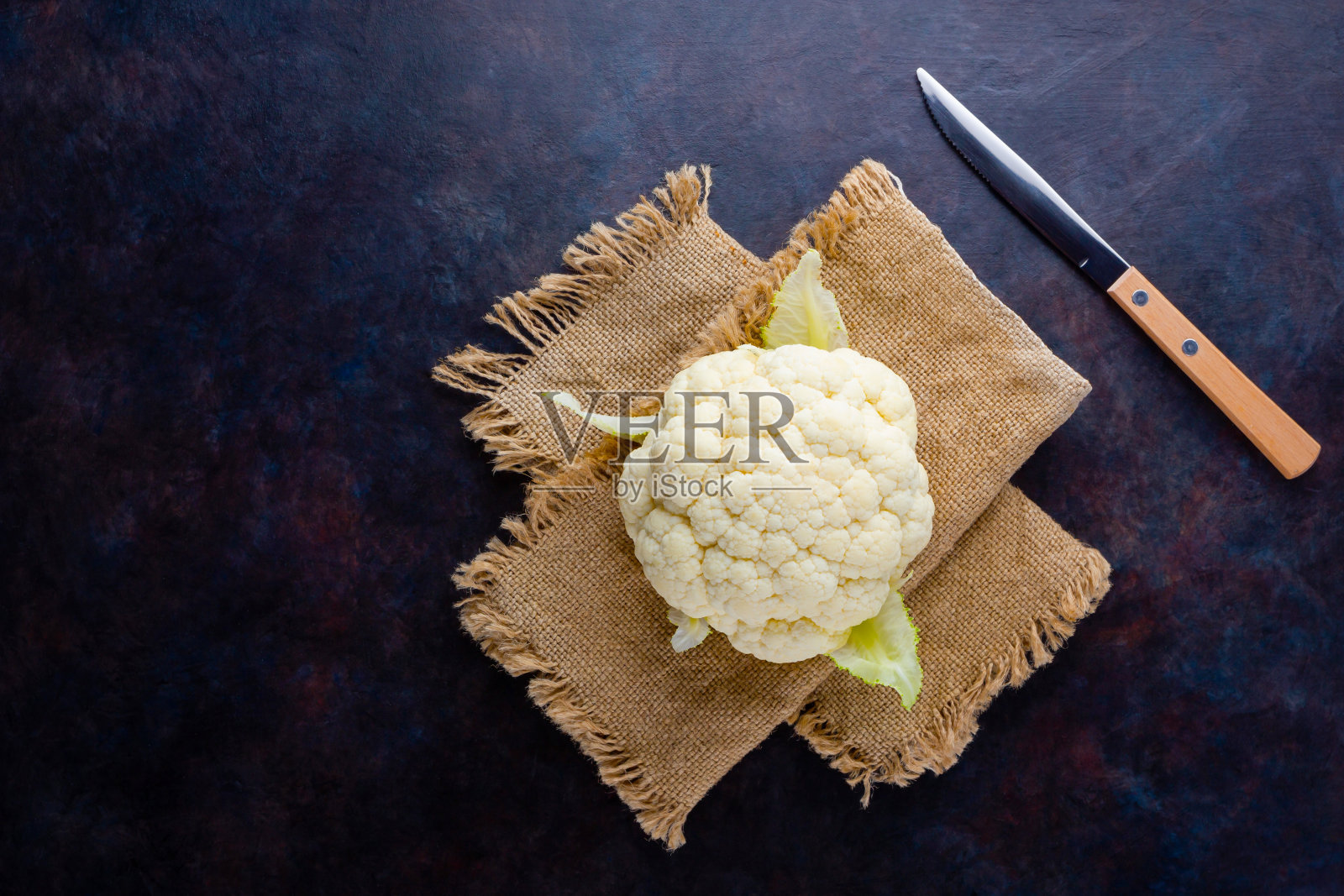深色背景上的有机菜花。花椰菜头放在麻袋和刀上。有机食品。乡村风格。本空间照片摄影图片