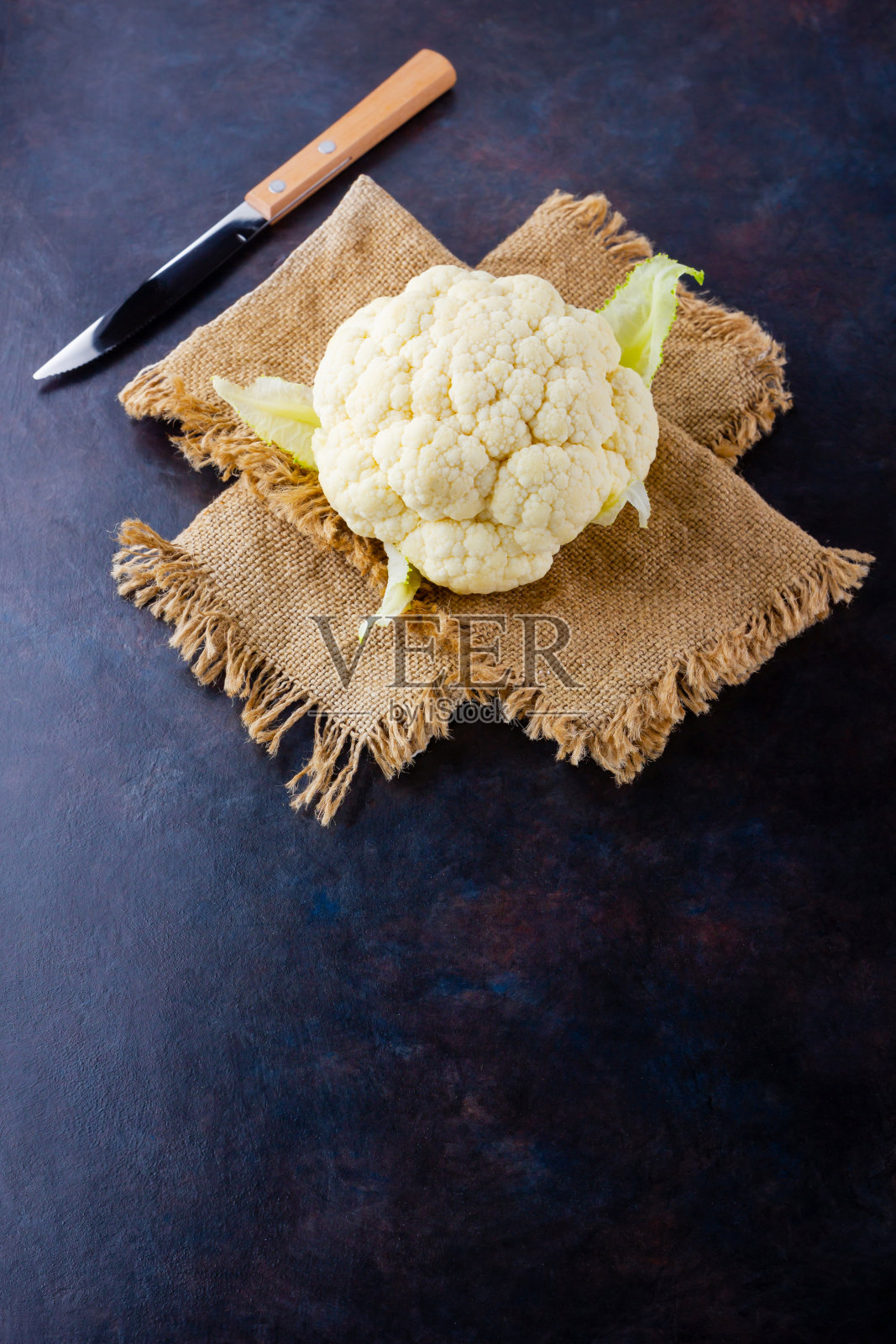 深色背景上的有机菜花。花椰菜头放在麻袋和刀上。有机食品。乡村风格。本空间照片摄影图片