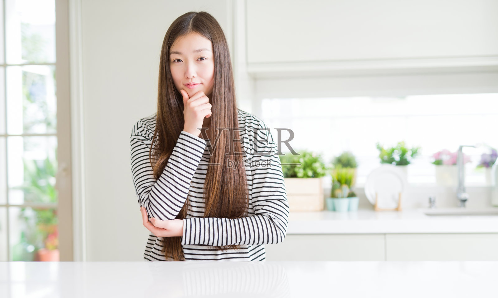 美丽的亚洲女人穿着条纹毛衣在镜头前看起来很自信，双臂交叉，手放在下巴上。积极的思考。照片摄影图片