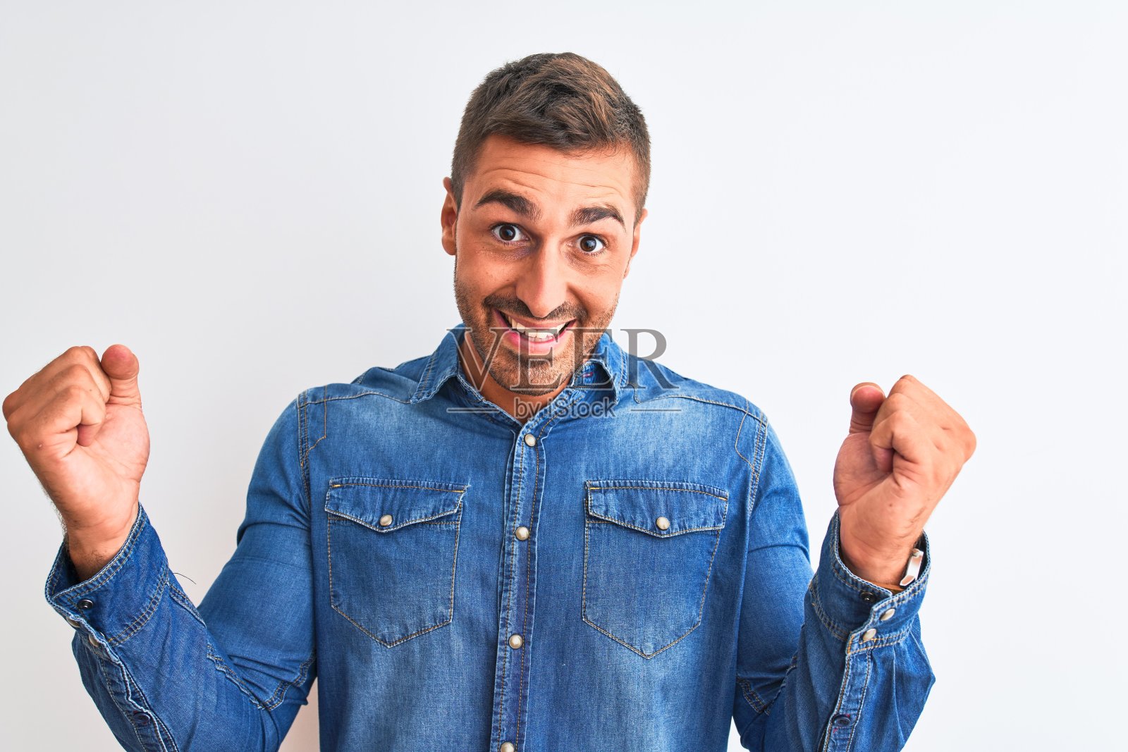 年轻英俊的男子穿着牛仔夹克站在孤立的背景庆祝惊讶和惊讶的成功，举起手臂，睁大眼睛。赢家的概念。照片摄影图片