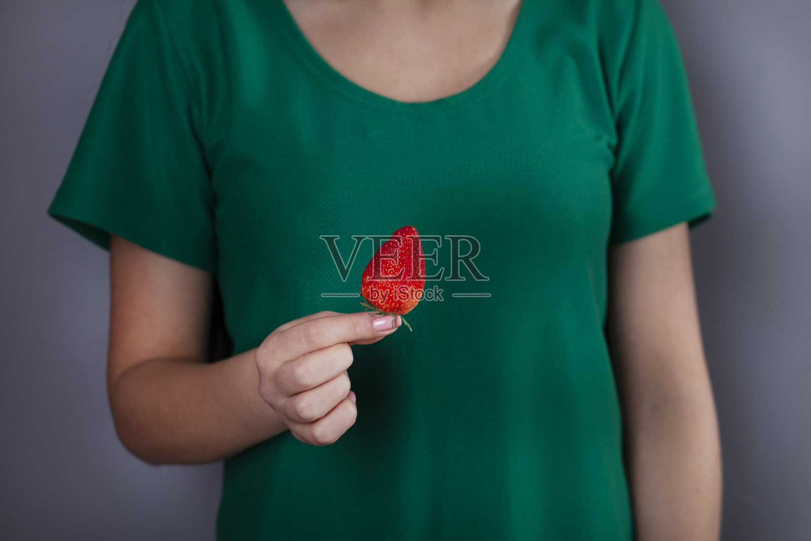 在灰色的背景下，一个女人手拿着草莓照片摄影图片