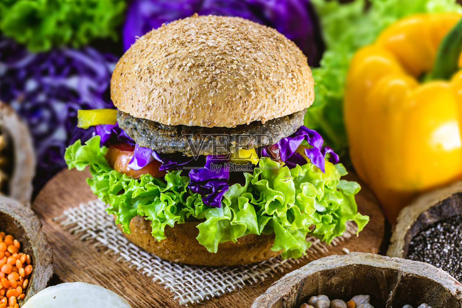 大的烤素食汉堡，由鹰嘴豆和大豆和蛋白质制成。健康素食的生活理念。五颜六色的食物，辣椒，红卷心菜，西红柿，洋葱，鹰嘴豆，大豆，生菜和碱液照片摄影图片