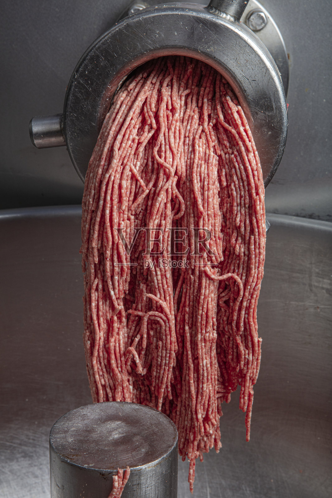 在食品加工厂，不明身份的屠夫手持装满生红肉碎末的托盘离开机器照片摄影图片