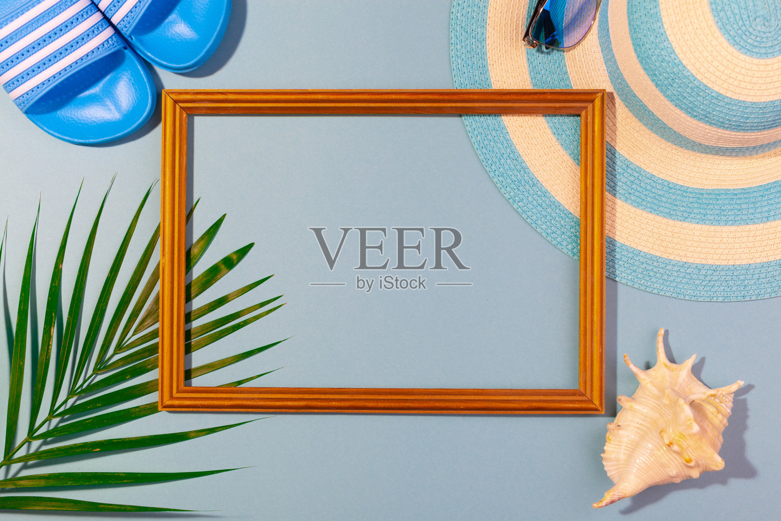 顶视图条纹蓝色帽子，太阳镜，人字拖，棕榈叶，贝壳和框架度假照片的蓝绿色背景。概念海滩度假，海上旅游，温暖阳光灿烂的夏天。复制粘贴照片摄影图片