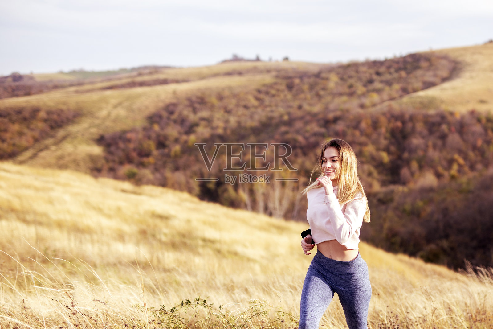 穿着运动服的女人在干燥的草地和林间空地的背景下奔跑照片摄影图片