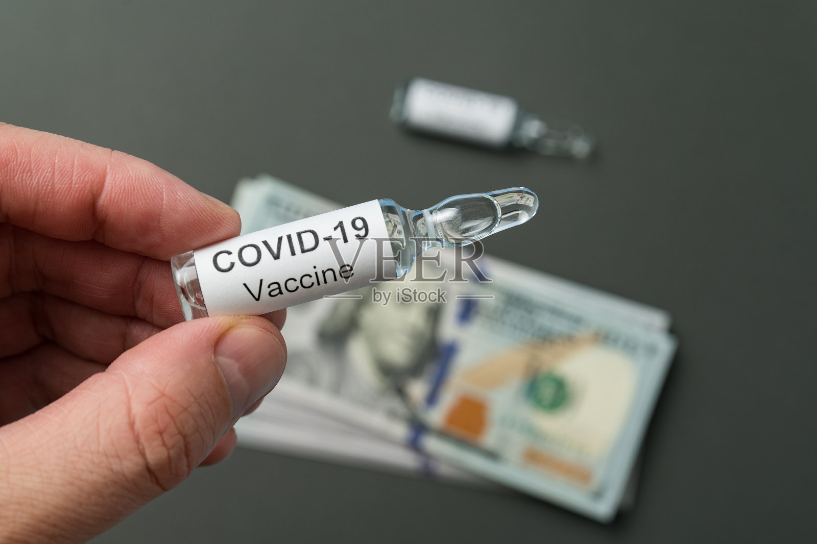 手持一个标有Covid-19货币背景标签的小瓶。新型冠状病毒传染病疫苗费用。照片摄影图片