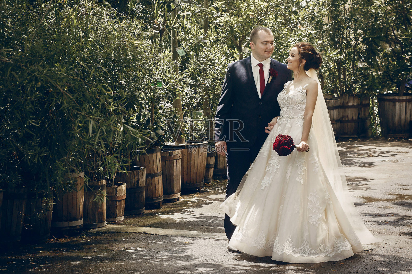 浪漫的新婚夫妇在公园散步，英俊的新郎和幸福美丽的新娘手牵花束在阳光明媚的植物园照片摄影图片