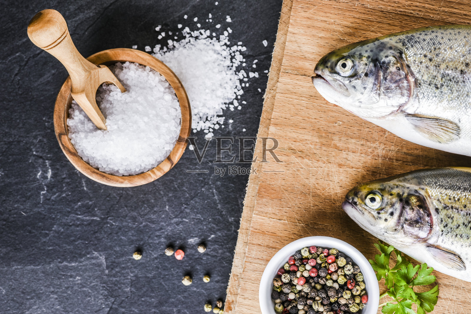 新鲜的彩虹鳟鱼放在木板上，放在深色的石桌上，加盐，胡椒，照片摄影图片