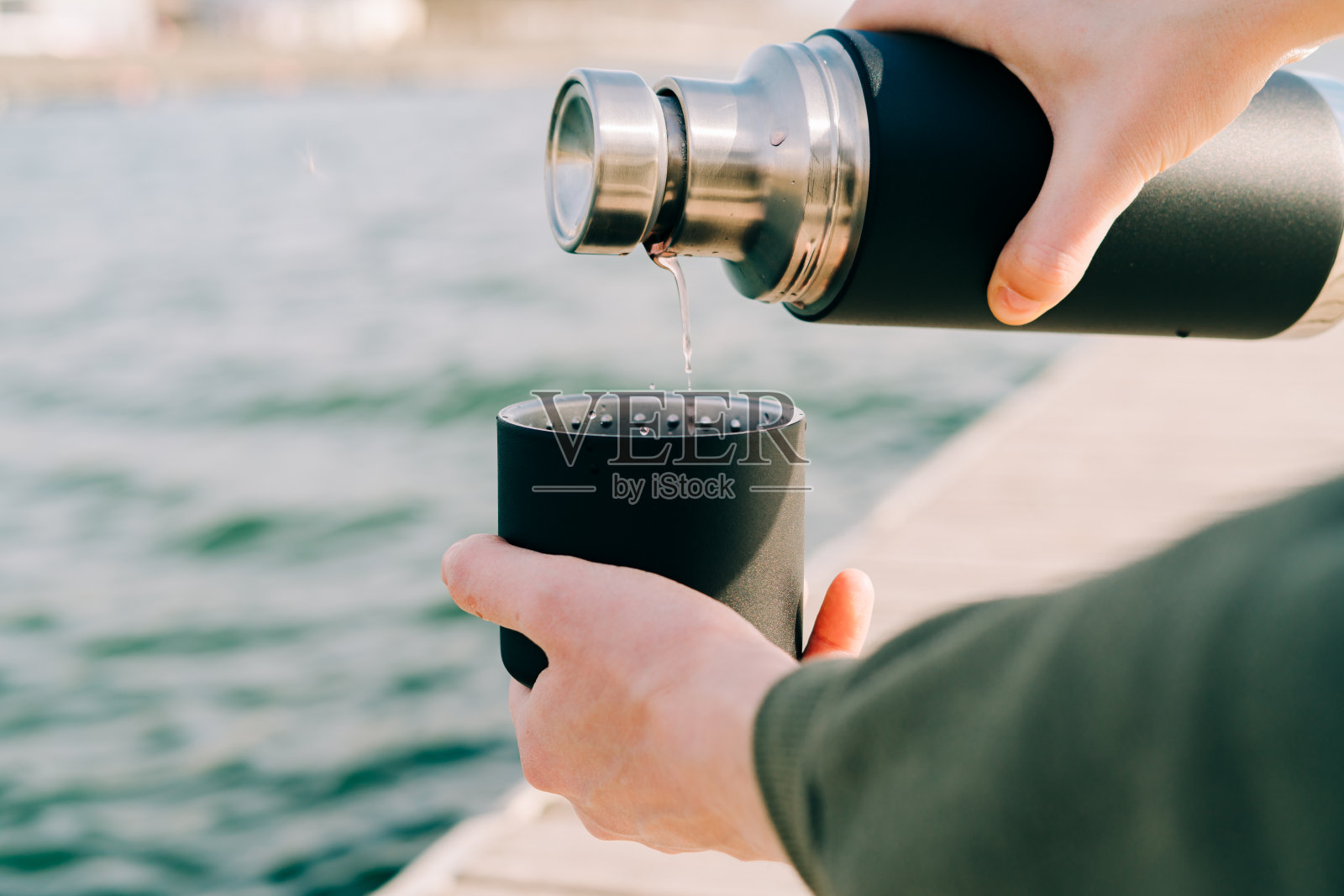 在一个阳光明媚的春日，在湖边的户外，这名男子拿着一个黑色时尚的环保不锈钢保温瓶，把热茶倒进一个大杯子里照片摄影图片