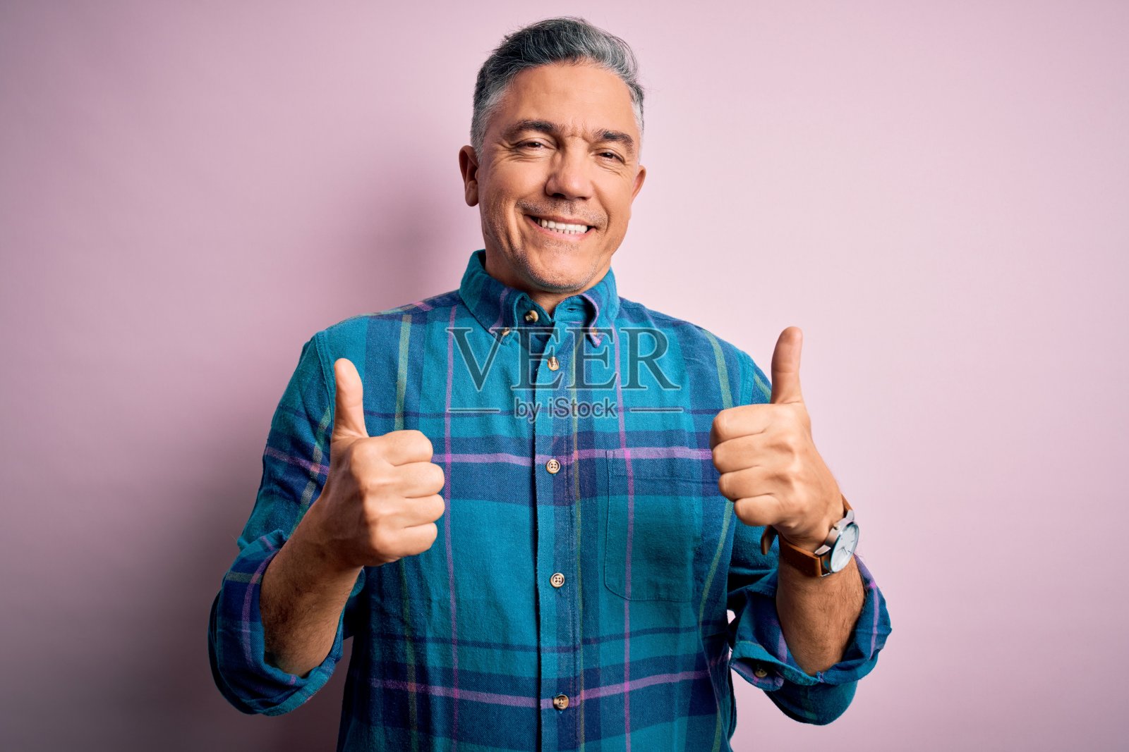 中年英俊灰发男子在粉红色背景前，竖起大拇指，面带微笑照片摄影图片