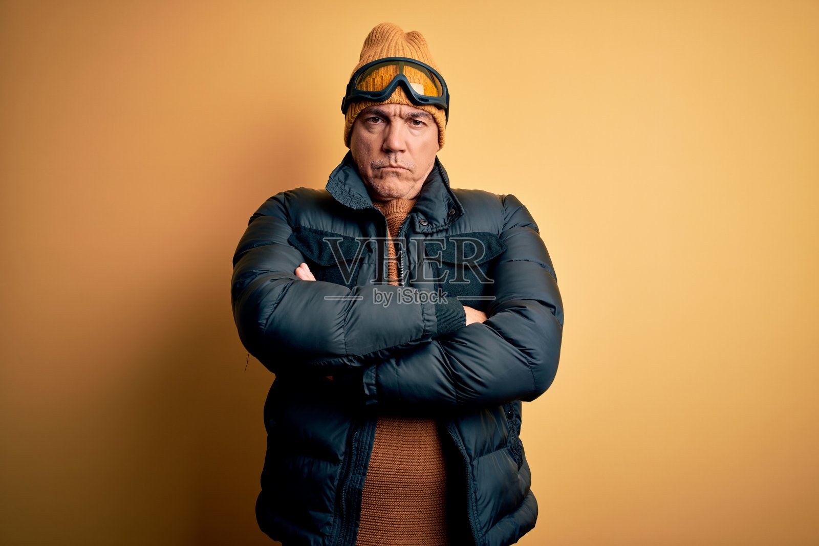 英俊的中年银发滑雪者在度假时戴着滑雪镜，持怀疑和紧张的态度，脸上带着不赞成的表情，双臂交叉照片摄影图片
