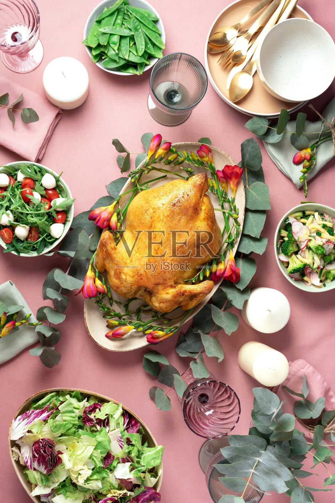 节日家庭餐桌。上菜的盘子，碗与沙拉和蔬菜菜肴，零食，整烤鸡，桉树花在粉红色破旧的背景。情人节，妇女节，母亲节，婚礼早午餐，节日家庭午餐照片摄影图片