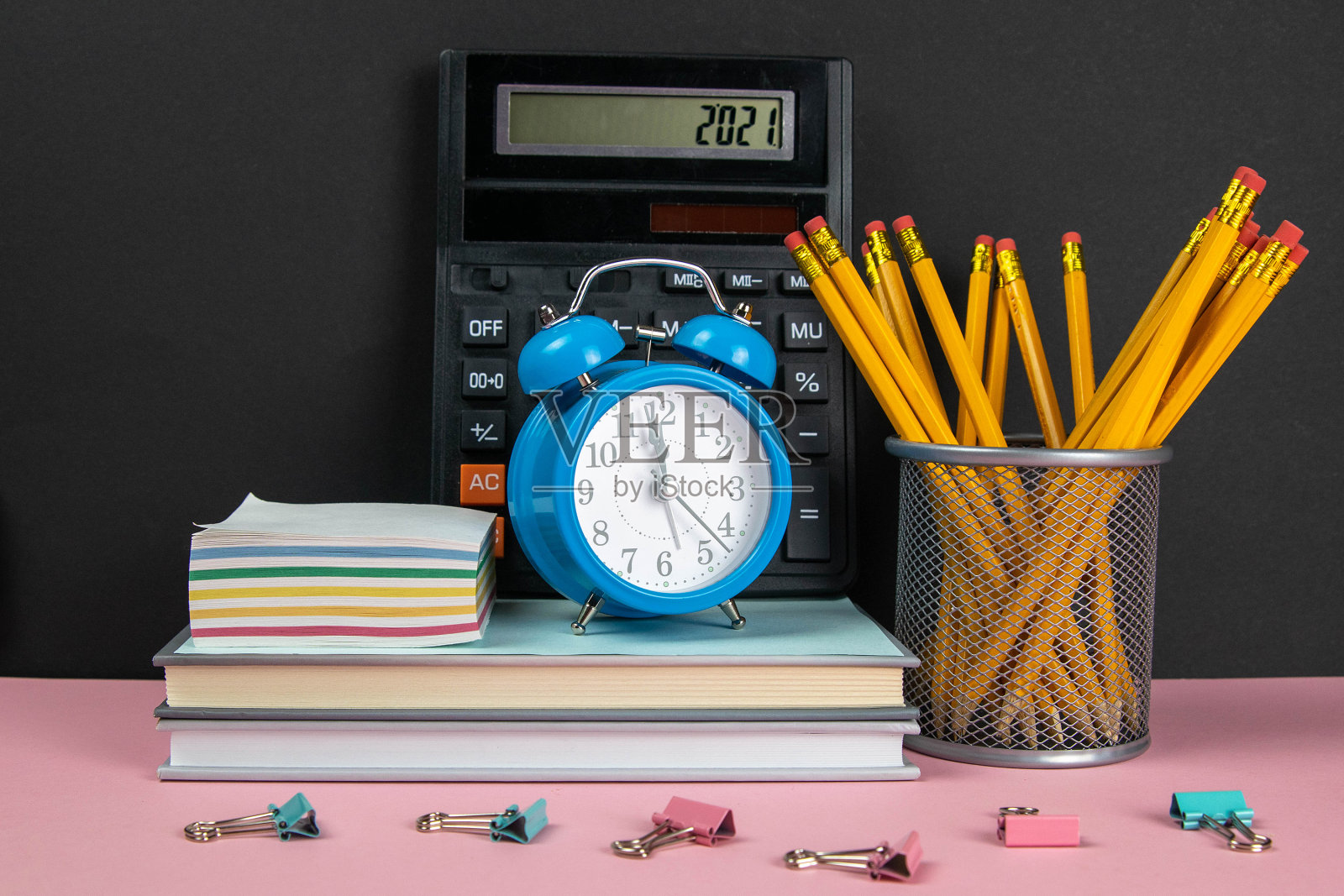 在一堆书上有一个计算器，一个时钟和笔记单，旁边是一玻璃杯铅笔照片摄影图片
