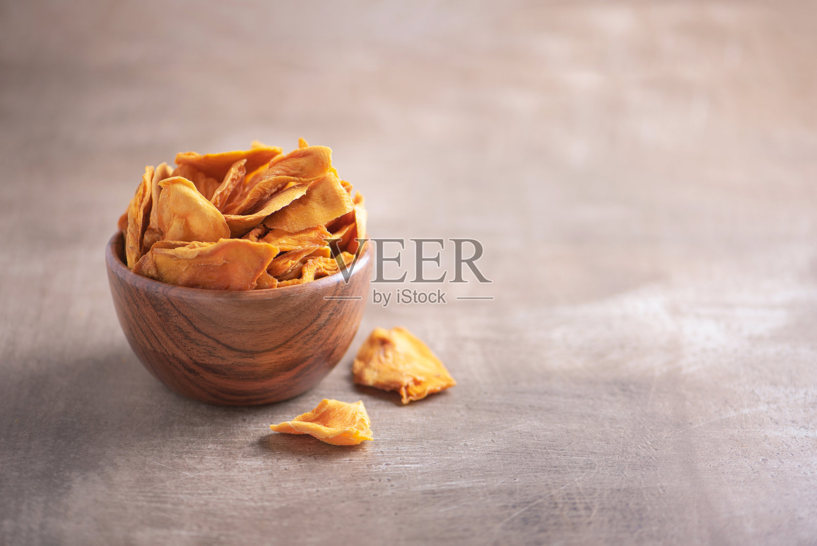 干芒果木碗木纹理背景。副本的空间。超级食物，素食，素食的概念。宏橙干芒果片，选择性聚焦。健康的零食。照片摄影图片