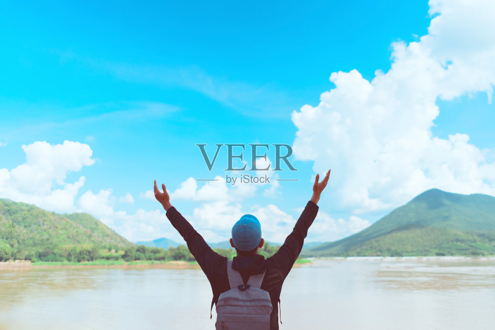 快乐的男人在河流上举起手，背景是蓝天白云和山脉抽象图案照片摄影图片