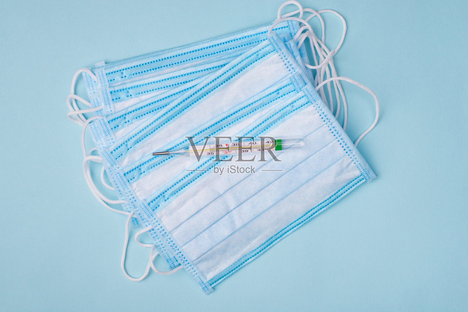 自我隔离首先症状危险概念。上面是一堆医用口罩和水银温度计的特写照片，孤立在蓝色背景上照片摄影图片